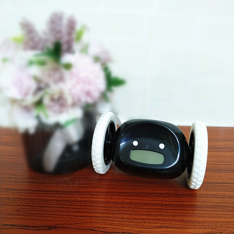 Black electronic device with wheels on a wooden surface, blurred flowers in the background