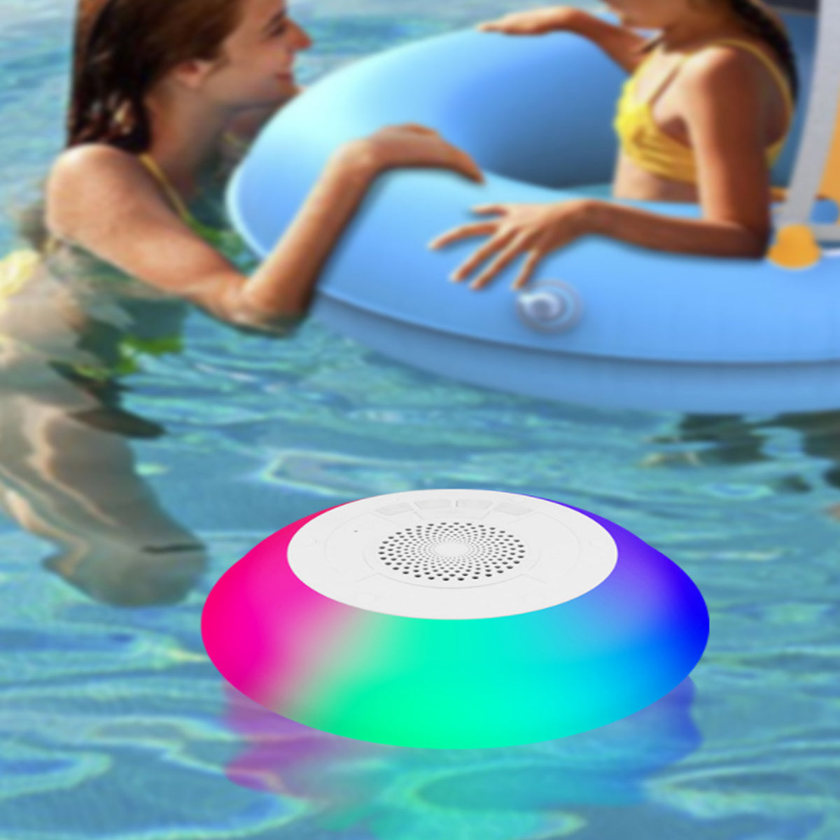 Colorful waterproof speaker floating in water with people on an inflatable ring in the background.