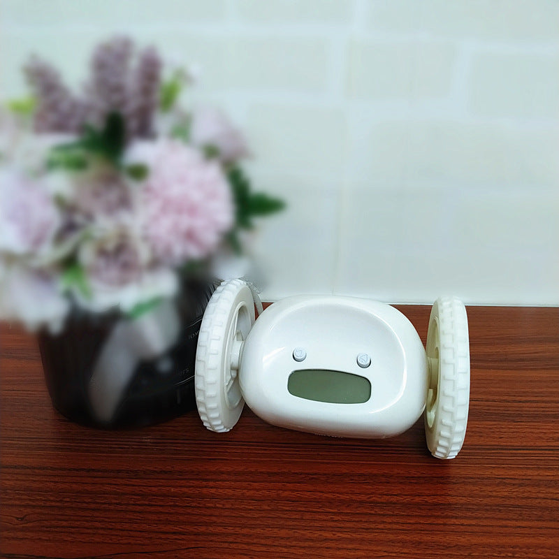 Small electronic device with wheels on a wooden surface with flowers in the background
