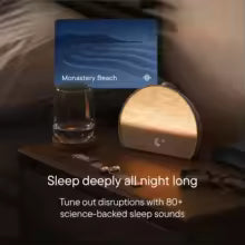 Sleep aid device with screen displaying 'Monastery Beach' on a bedside table.