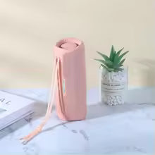 Pink cylindrical container on a white surface with a plant and book in the background